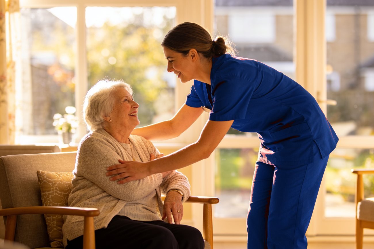 A MAP HealthCare HCA in navy scrubs smiling with an elderly resident in a Bristol care home lounge